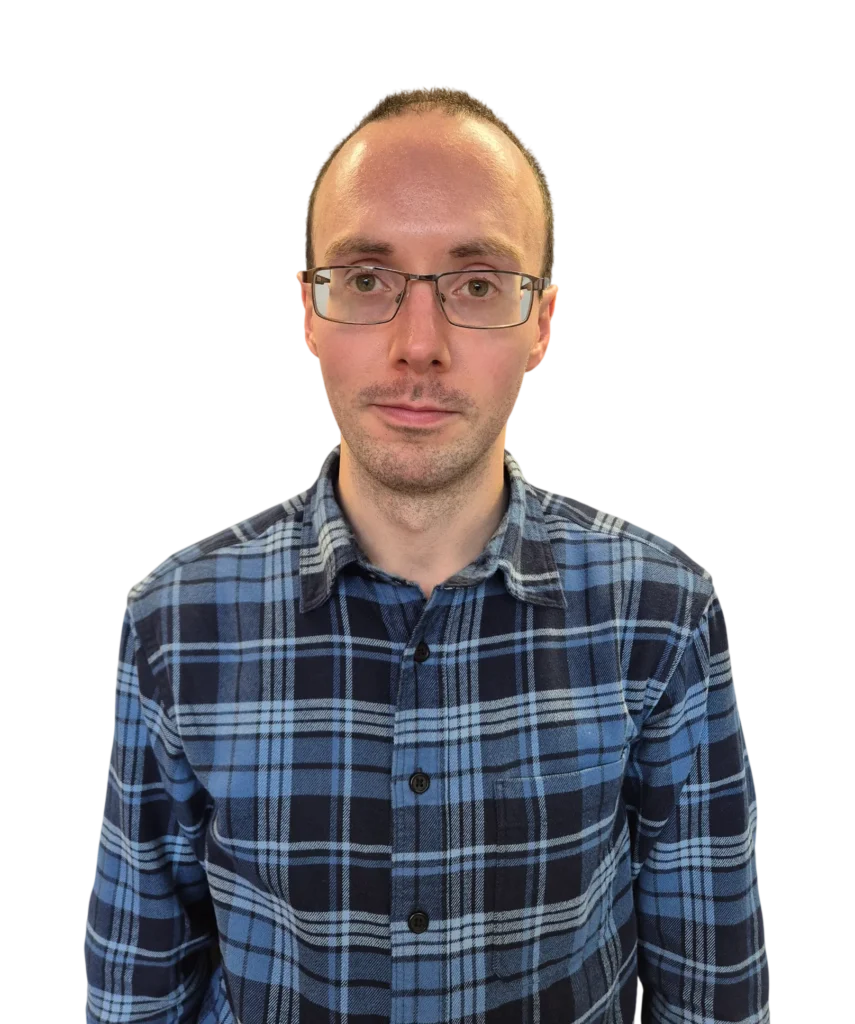 Man in blue plaid shirt and glasses looking at camera on white background.