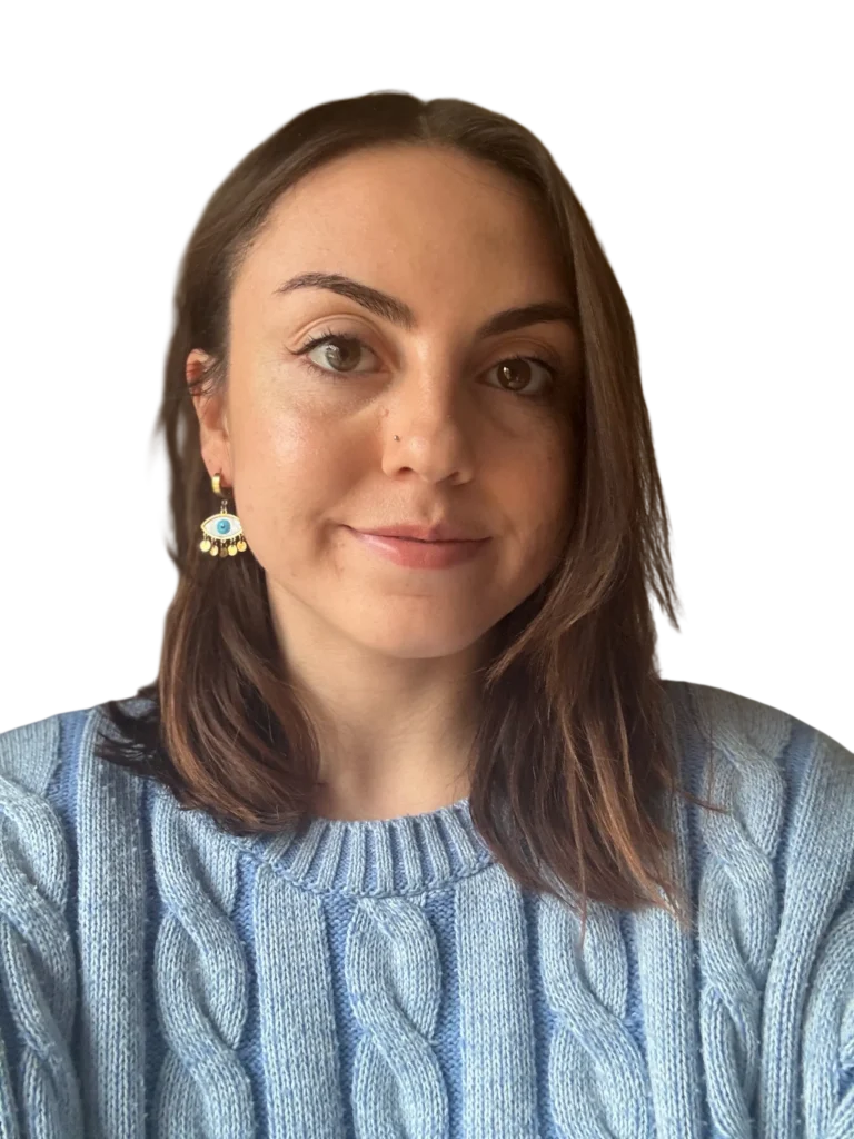 Portrait of a woman in a blue sweater with eye-shaped earrings, neutral background.