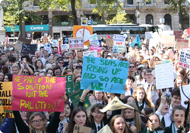 Crowd of climate activists holding signs at a protest advocating for environmental change and action against pollution.