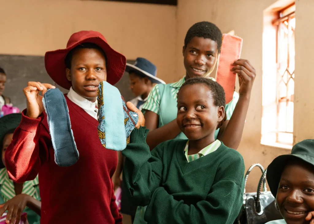 Students proudly display handmade reusable sanitary pads in a classroom, promoting menstrual hygiene education.