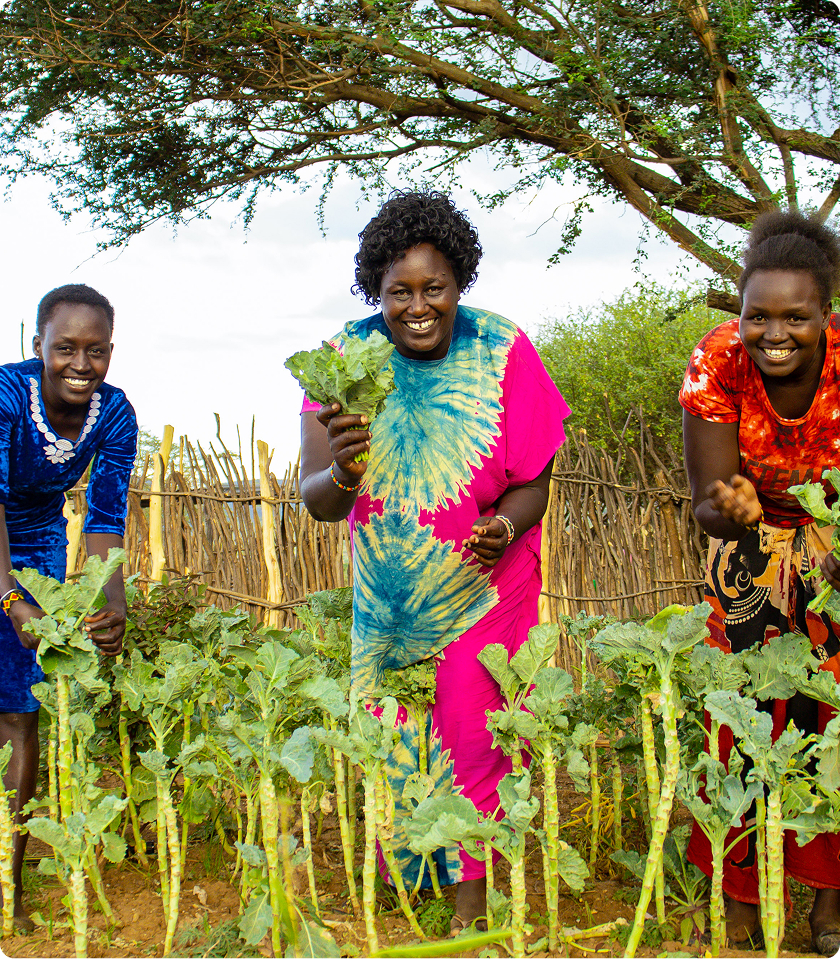 Women happily tending to crops in a vibrant garden, showcasing sustainable farming practices.